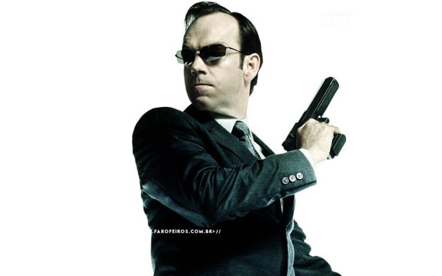 Agente Smith dos filmes Matrix sendo visto de lado. Ele olha para trás enquanto empunha sua pistola em uma cena de ação. O personagem aparece isolado na imagem com fundo branco. Na parte inferior, a marca d'água do site www.farofeiros.com.br