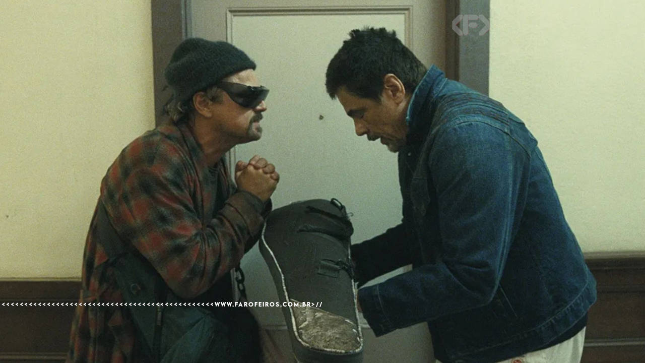 Benício Del Toro (Sensei) e Leo diCaprio (Pat/Bob) em cena de Uma Batalha Atrás da Outra, com Sensei entregando uma arma para Bob dentro de uma caixa de violão.