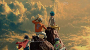 Ilustração animada da capa do single "The Hardest Thing" do Gorillaz. Os quatro membros da banda estão sobre uma formação rochosa isolada diante de um céu com nuvens douradas. De costas no centro, Russel de moletom laranja e boné, e 2-D de cabelo azul e calça amarela. Abaixo, à esquerda Noodle com capa vermelha, e à direita, Murdoc de pele verde mexendo no celular. Na parte inferior, a marca d'água do site www.farofeiros.com.br