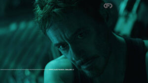 Cena do filme Vingadores: Ultimato com iluminação esverdeada. Close no rosto de Tony Stark, interpretado por Robert Downey Jr., com expressão abatida e exausta, olhando para baixo. Na parte inferior, a marca d'água do site www.farofeiros.com.br