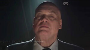 Close dramático de Wilson Fisk em ambiente escuro, com iluminação intensa sobre o rosto, transmitindo uma presença ameaçadora. Captura da série do Demolidor.