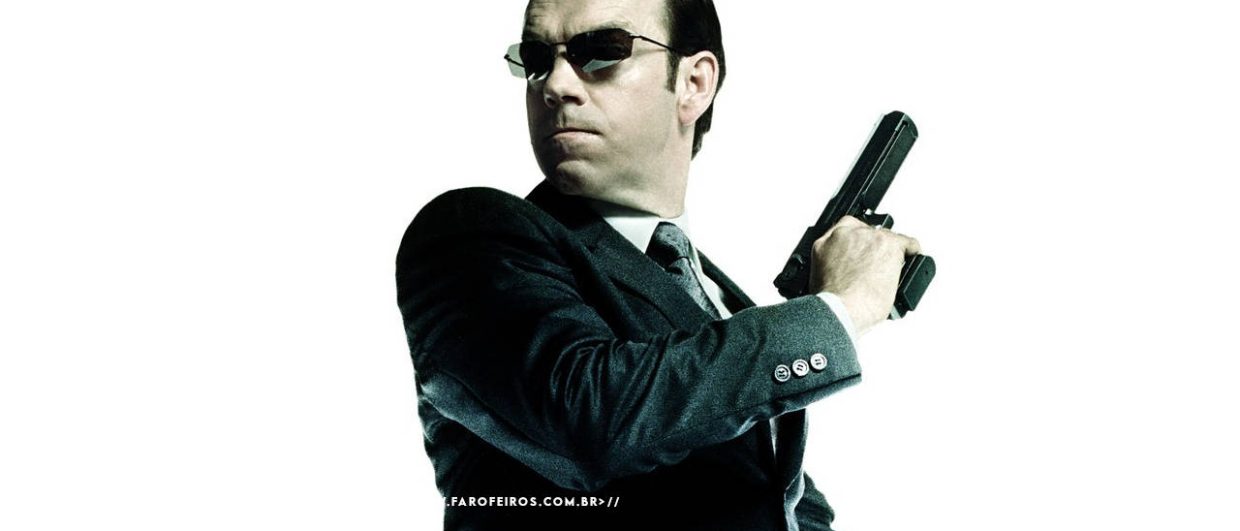 Agente Smith dos filmes Matrix sendo visto de lado. Ele olha para trás enquanto empunha sua pistola em uma cena de ação. O personagem aparece isolado na imagem com fundo branco. Na parte inferior, a marca d'água do site www.farofeiros.com.br