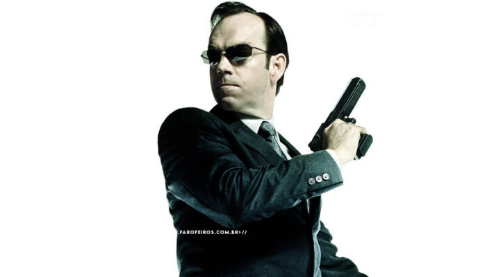 Agente Smith dos filmes Matrix sendo visto de lado. Ele olha para trás enquanto empunha sua pistola em uma cena de ação. O personagem aparece isolado na imagem com fundo branco. Na parte inferior, a marca d'água do site www.farofeiros.com.br