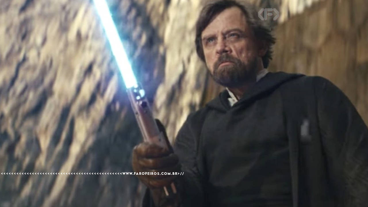 Cena de Star Wars: Os Últimos Jedi. Luke Skywalker mais velho, com barba e manto escuro, segurando seu sabre de luz azul erguido com uma mão, com expressão séria. Ao fundo, paredes rochosas escuras. Na parte inferior, a marca d'água do site www.farofeiros.com.br