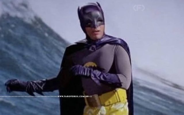 Batman de Adam West surfando de sunga amarela em um corte de cena da cintura para cima e braços jogados para a esquerda.