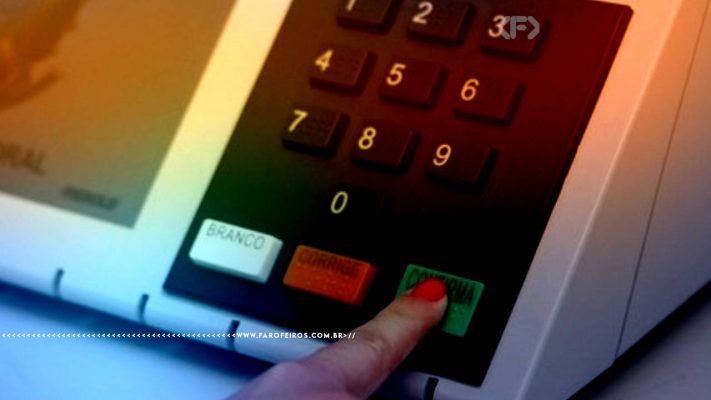 Fotografia focando números da urna eletrônica brasileira com um dedo com unha vermelha apertando o botão de CONFIRMA